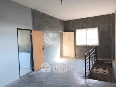 Spacious industrial-style interior with concrete walls and floors, featuring a large window and modern railing.