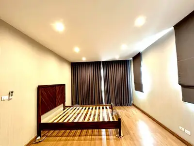 Spacious bedroom with wooden flooring and modern lighting, featuring a large bed frame and elegant curtains.