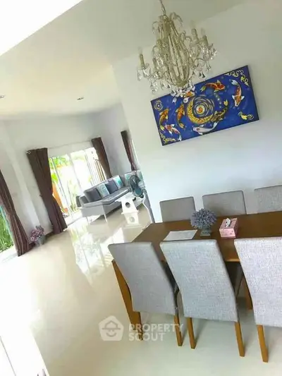 Elegant dining area with chandelier and art, open to bright living room with garden view.