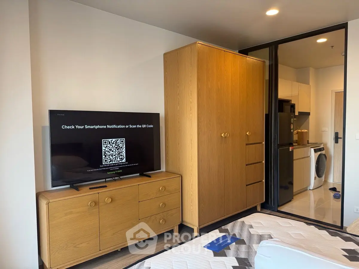 Modern bedroom with wooden furniture and view into kitchen with appliances
