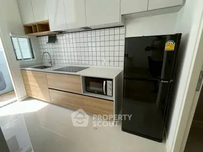 Modern kitchen with sleek cabinetry, built-in microwave, and black refrigerator in a stylish apartment.