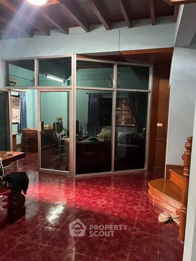 Spacious living area with red tiled floor and glass partition, featuring wooden staircase.