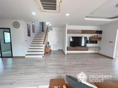 Spacious living room with modern design, elegant wood flooring, and an integrated entertainment unit, leading to a stylish staircase.