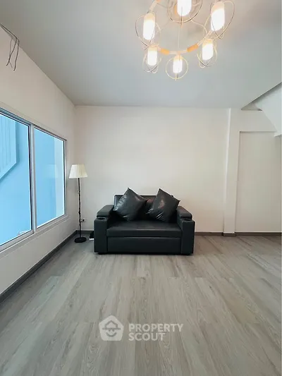 Modern living room with sleek black sofa and elegant lighting, featuring large window and stylish flooring.