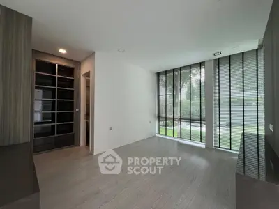 Spacious modern room with large windows and garden view, featuring sleek wooden flooring and built-in storage.
