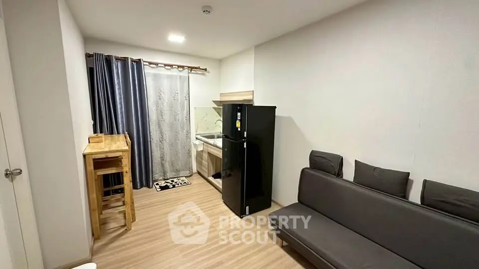 Modern studio apartment with compact kitchen and cozy living area, featuring sleek black fridge and stylish decor.