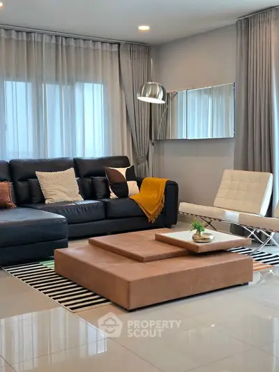 Modern living room with stylish furniture and elegant decor, featuring a black sofa and contemporary lighting.