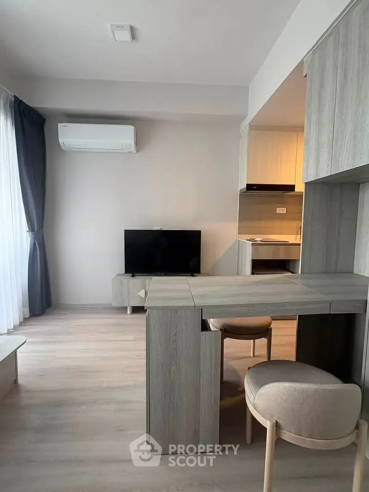 Modern living room with sleek furniture and open kitchen layout, featuring a wall-mounted TV and air conditioning.