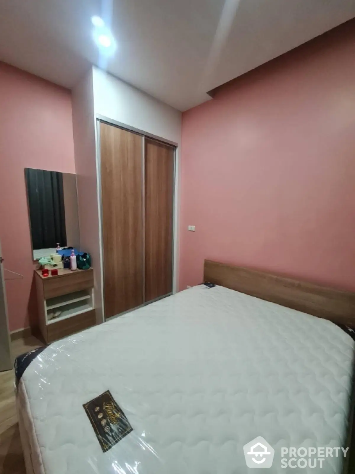 Cozy bedroom with pink walls and wooden wardrobe, perfect for relaxation.