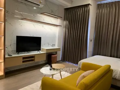 Modern studio apartment with stylish decor and cozy ambiance, featuring a yellow sofa and wall-mounted TV.