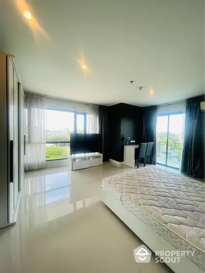 Spacious bedroom with large windows and natural light in modern apartment.