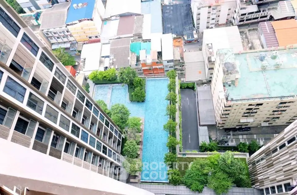 Stunning aerial view of modern high-rise building with luxurious pool and lush greenery in urban setting.