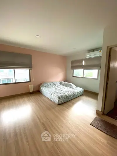 Spacious bedroom with large windows and wooden flooring in modern apartment