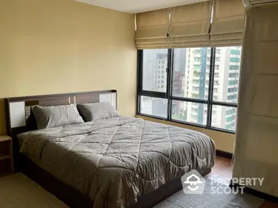 Spacious bedroom with large windows offering city views in modern apartment.