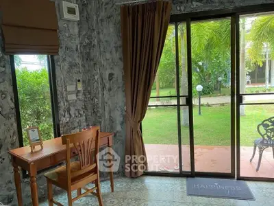 Charming interior with garden view, featuring a cozy study area and sliding glass doors opening to lush greenery.