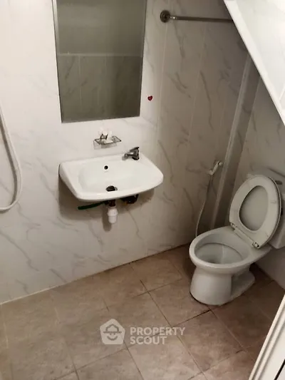 Compact bathroom with white fixtures and tiled walls, featuring a sink, toilet, and shower area.