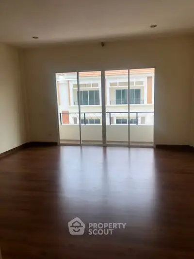 Spacious empty living room with large windows and wooden flooring, perfect for customization.