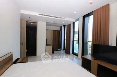 Modern bedroom with large windows and city view, featuring sleek furniture and neutral tones.