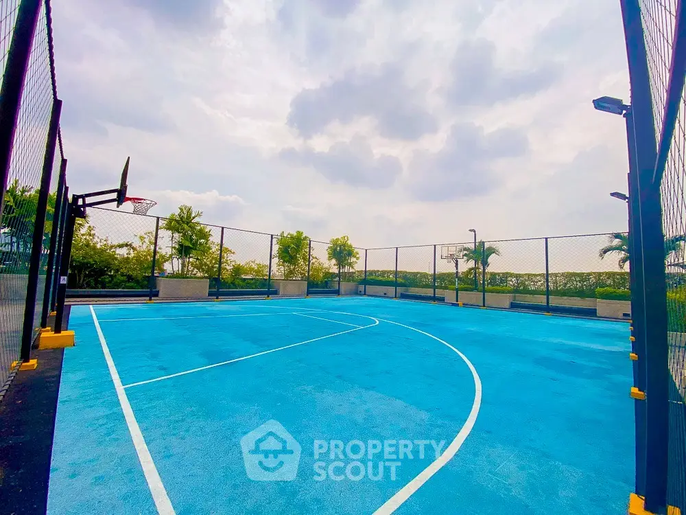 Spacious outdoor basketball court with clear blue sky and lush greenery, perfect for sports enthusiasts.