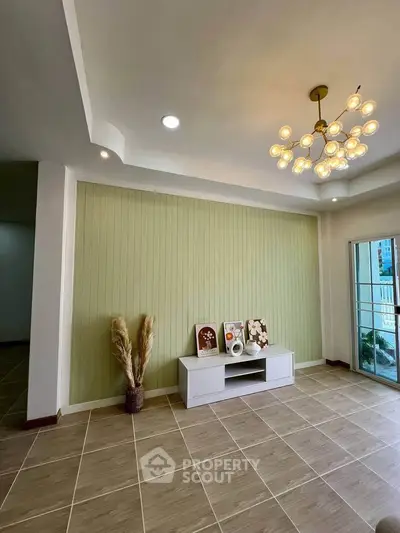 Stylish living room with modern chandelier and elegant decor, featuring a light green accent wall and balcony access.