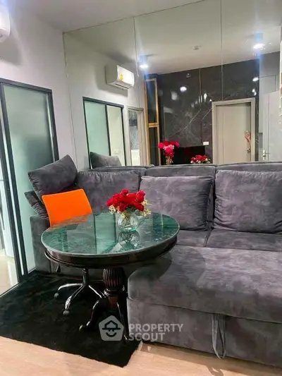 Stylish living room with modern gray sofa and elegant glass table, accented by vibrant red flowers.
