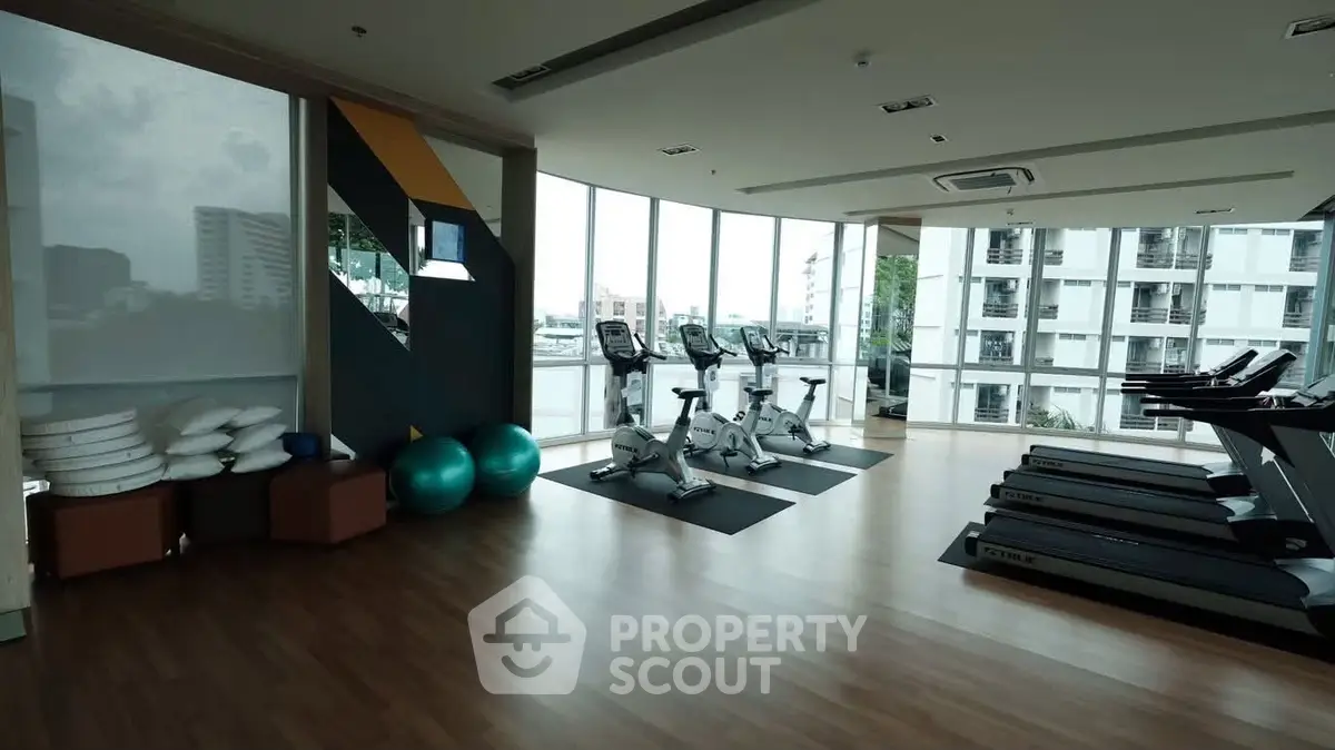 Spacious gym with modern equipment and city view in luxury apartment building.