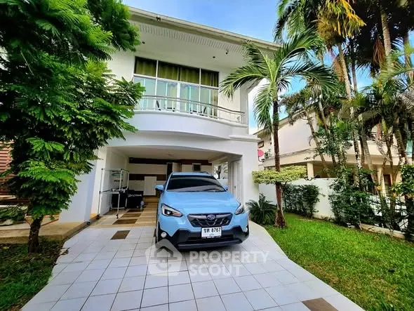 Charming two-story house with lush garden and driveway parking in tropical setting.
