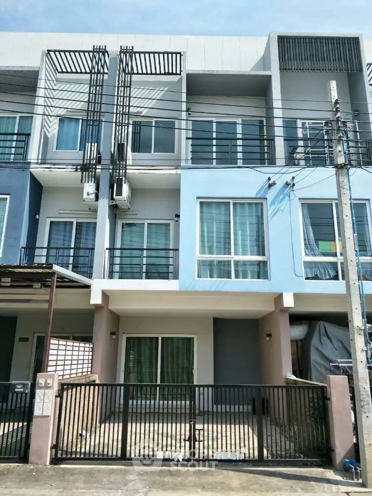 Modern townhouse with a sleek blue and gray facade, featuring large windows and a cozy entrance porch, ideal for urban living.