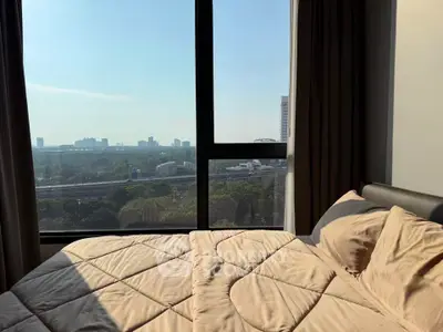 Cozy bedroom with large window offering stunning cityscape view, perfect for urban living.