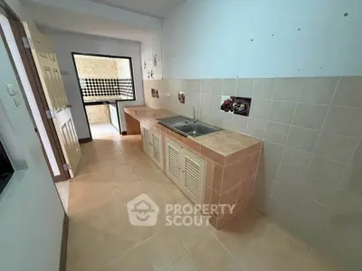 Spacious kitchen with tiled countertops and open layout leading to balcony.