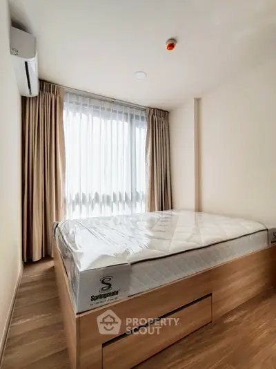 Modern bedroom with natural light and stylish wooden flooring, featuring a comfortable bed and elegant curtains.