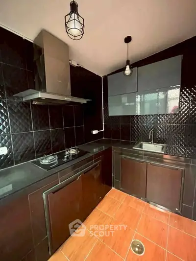 Modern kitchen with black tiles and gas stove, featuring sleek cabinetry and stylish lighting.