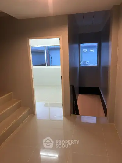 Modern interior with sleek staircase and polished tile flooring, leading to a bright open space.