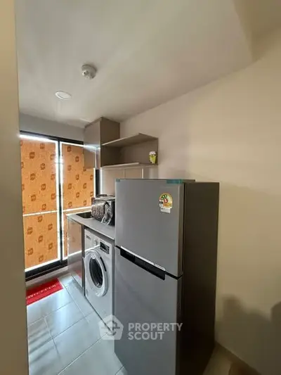 Modern kitchen with fridge, washing machine, and ample storage space.