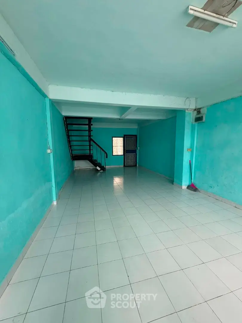 Spacious open-plan room with teal walls and tiled flooring, featuring a staircase and natural light.