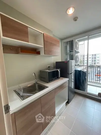Modern kitchen with sleek cabinetry and balcony view, featuring microwave and refrigerator.