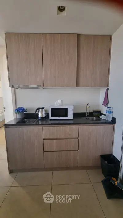 Modern compact kitchen with wooden cabinets, microwave, and sleek black countertop.