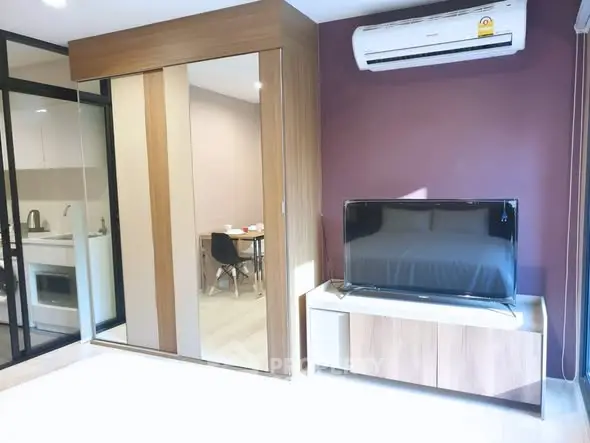 Modern living room with sleek TV setup and air conditioning, adjacent to a stylish kitchen.