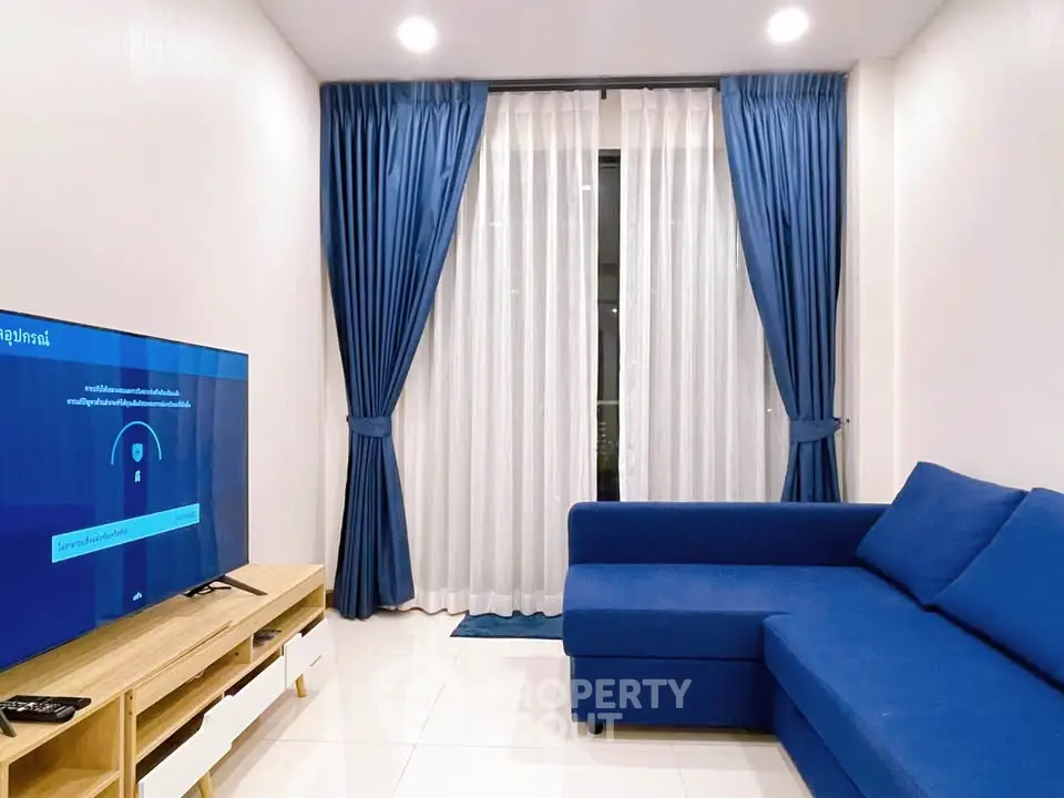 Modern living room with blue sofa and curtains, featuring a sleek TV setup and bright lighting.