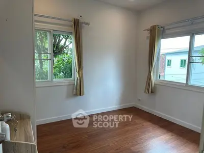 Bright empty room with wooden flooring and large windows offering garden views.