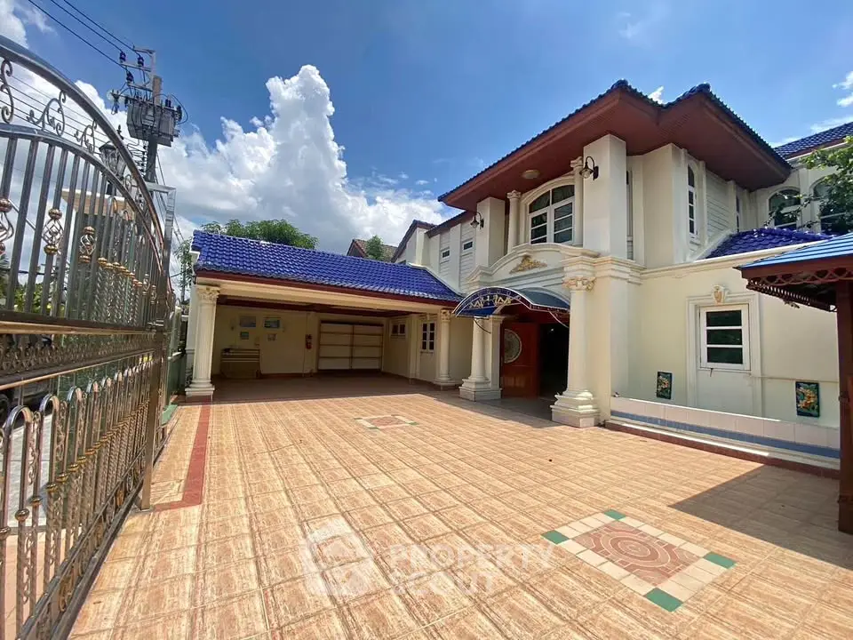 Stunning two-story house with blue roof and spacious tiled driveway under a clear sky.