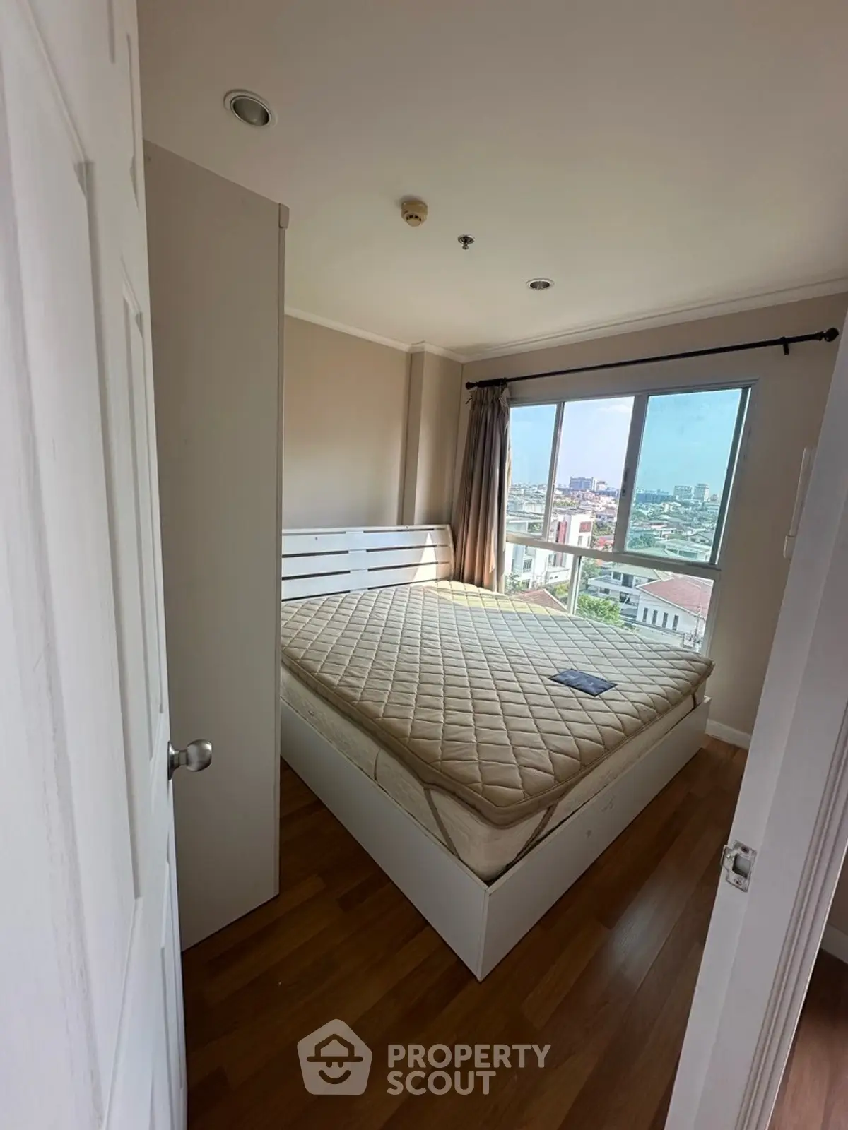 Cozy bedroom with city view and natural light, featuring a comfortable bed and wooden flooring.