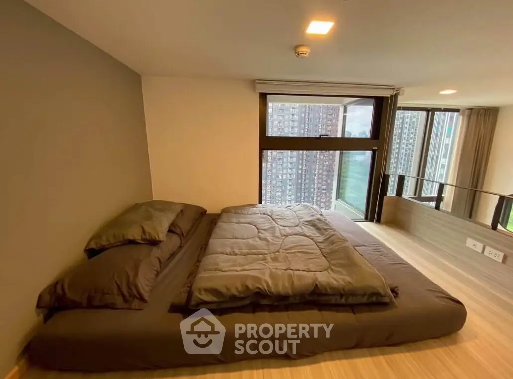 Modern bedroom with large window and city view, featuring a low-profile bed and sleek design.