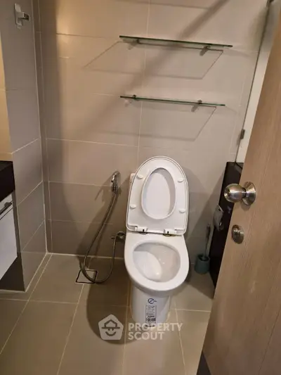 Modern bathroom with sleek fixtures and neutral tiles, featuring a toilet and bidet spray.