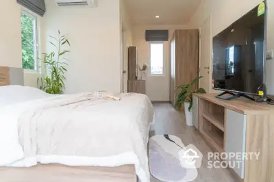 Modern bedroom with cozy decor and large TV, featuring natural light and stylish furniture.