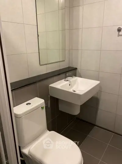 Modern bathroom with sleek sink and toilet, tiled walls and floor.
