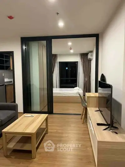 Modern living room with wooden flooring and sliding glass doors leading to a cozy bedroom.