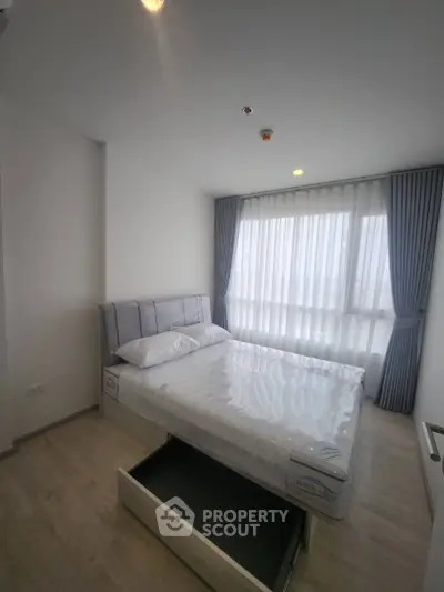 Modern bedroom with sleek design, featuring a comfortable bed and large window with elegant curtains.