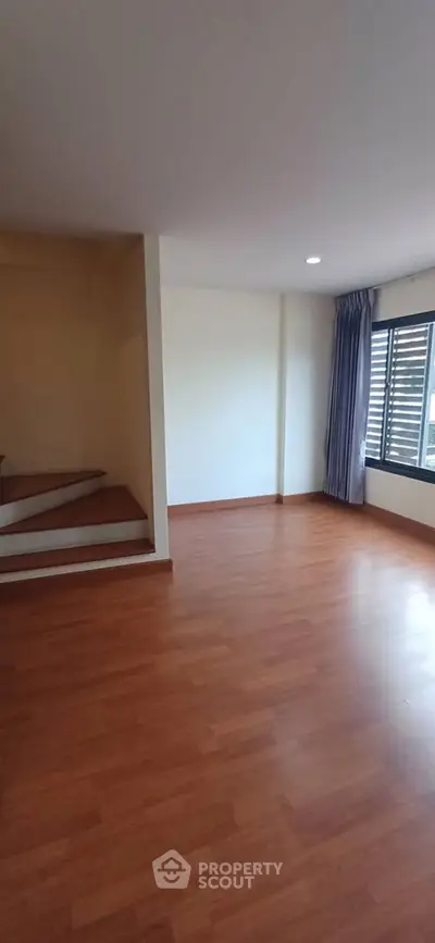 Spacious living room with wooden flooring and large window for natural light.