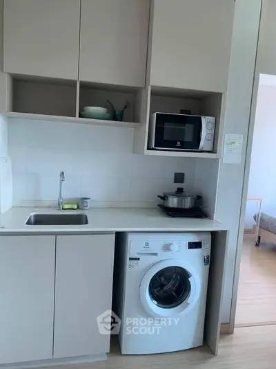 Compact kitchen with washing machine and microwave in modern apartment